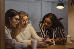 Three women in casual attire engaged in a business discussion over coffee in a cozy café setting.